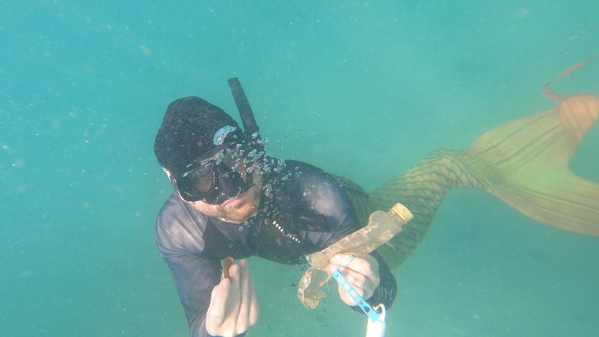 A mermaid picking up debris underwater for Mermaid Against Debris.